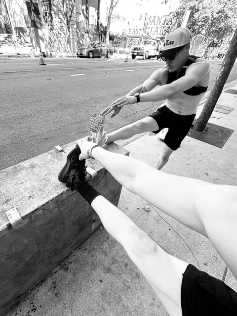 Man in cap and tank top stretching leg against urban tree and concrete, black and white street photography